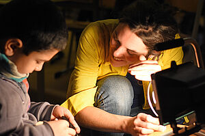 Eine Pädagogin und ein Junge arbeiten gemeinsam im Licht eines Baustrahlers