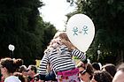 Kind mit Luftballon sitzt bei einer Demonstration auf den Schultern eines Elternteils