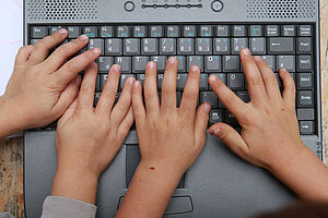 Kinderhände tippen auf einer Tastatur.