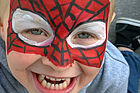 Ein Kind ist als Spider-Man rot und schwarz geschminkt. Es lacht mit offenem Mund.