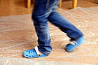 Füße eines Kindes in Hausschuhen, die über den Kita-Boden laufen.