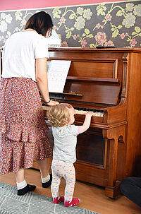Junghee Cho steht am Klavier, neben ihr ein kleines Kind, das auch auf die Tasten drückt