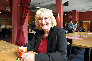 Sigrid van Essen sitzt mit einer Teetasse in der Hand an einem Tisch.