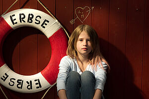 Ein Mädchen sitzt neben einem Rettungsring, auf dem Erbse steht.