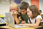 Drei Kinder sitzen vor einem Laptop.